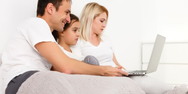 Photo happy family lies on bed and watching something on laptop.