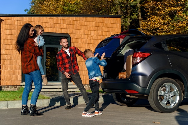 A happy family loads luggage into the trunk of a car when going on a family vacation.