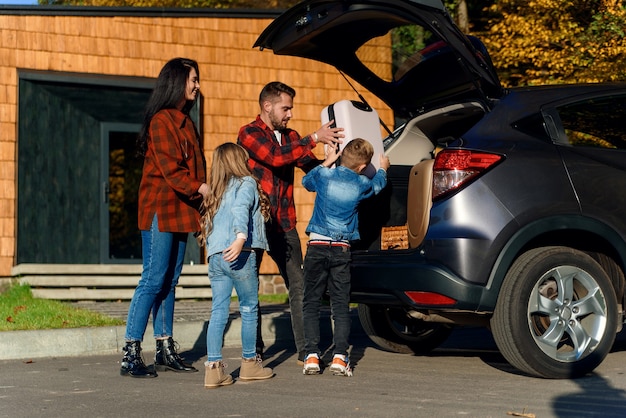 A happy family loads luggage into the trunk of a car when going on a family vacation.
