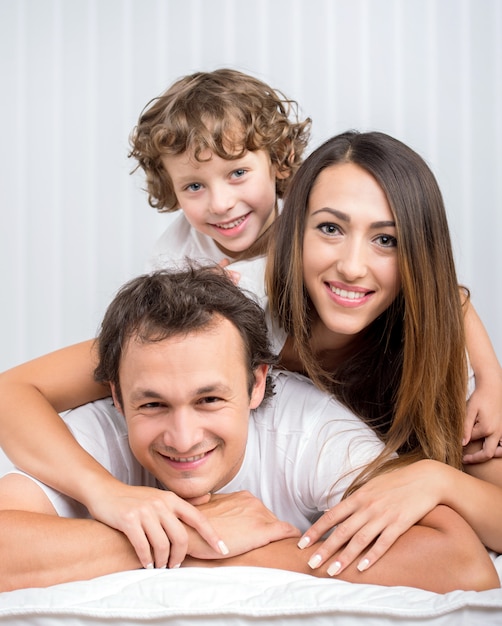 Happy family looking at the camera on their bed.