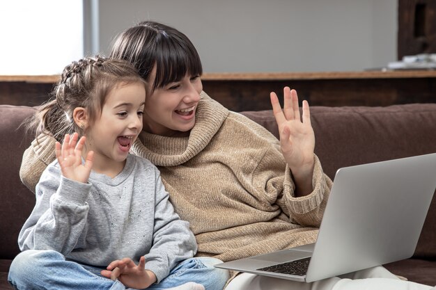 Happy family looking at laptop screen make distance video call. smiling mother and little girl talking to webcamera on internet chat.