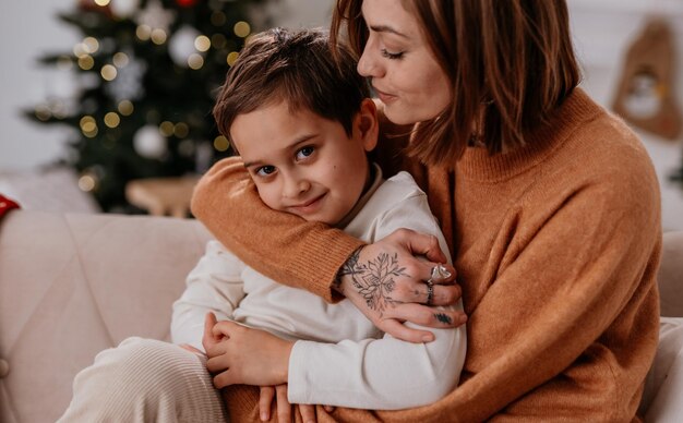 愛する母と息子の幸せな家族が自宅で居心地の良い冬の夜に抱き合い、微笑むかわいい男の子ルックイ