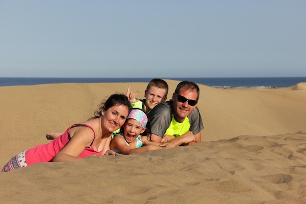 Famiglia felice sdraiata sulle dune di sabbia di maspalomas ritratto di giovani genitori e bambini in natura