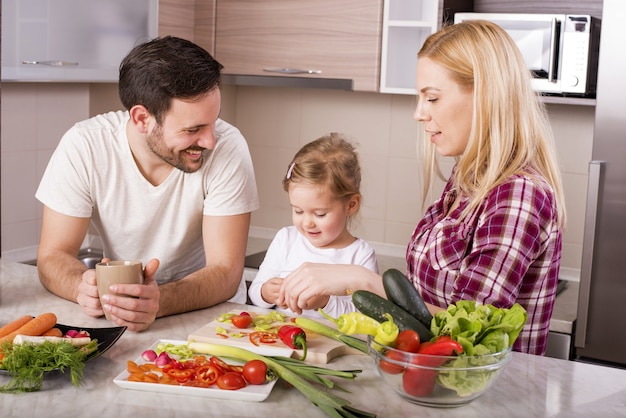 Фото Счастливая семья, готовящая салат из свежих овощей на кухонном столе