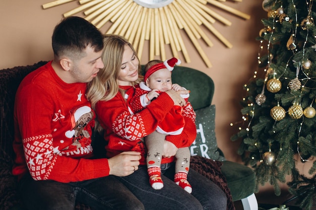 Happy family mom dad and little daughter in red traditional Christmas clothes spending time together near Christmas tree copy space