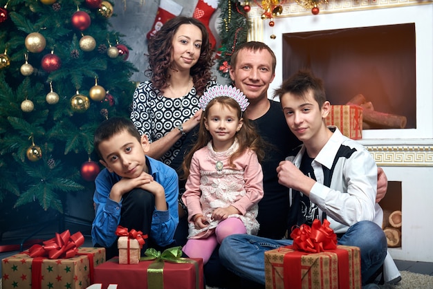 Foto famiglia felice: mamma, papà e tre figli davanti al camino per le vacanze invernali. vigilia di natale e capodanno.