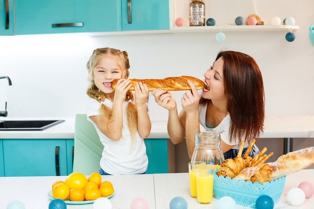 행복한 가족, 엄마와 딸은 다른 쪽에서 물고 있는 하나의 빵을 먹습니다. 부모와 자녀의 가족 관계
