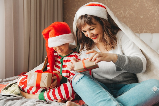 Happy family, mom and son, hugging and giving gifts in bed on Christmas morning. Christmas.