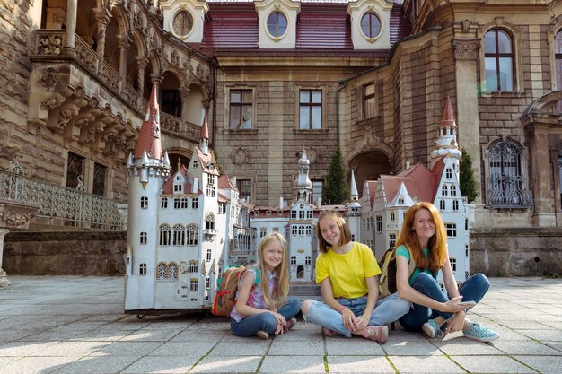 Happy family - mom and two daughters are sitting in a meadow Beautiful castle on the background