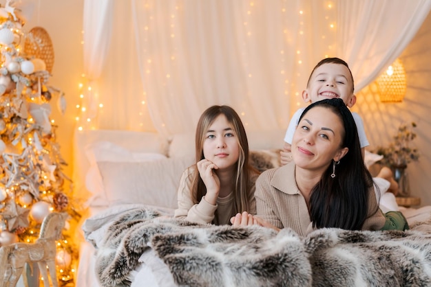 Happy family mom and two kids lying on bed waiting for christmas and laughing