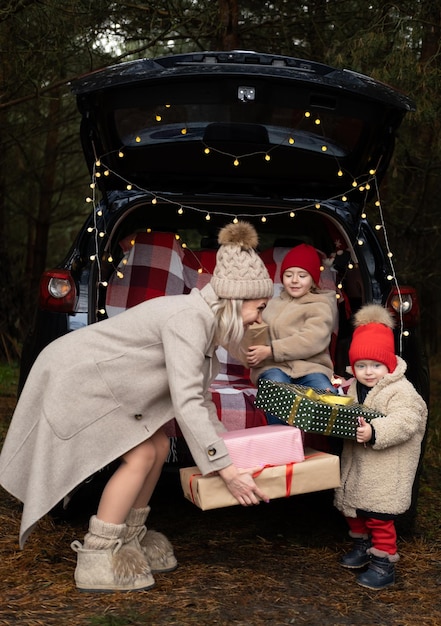 Happy family of mom and two kids with Christmas gift boxes sitting in christmas decorated car