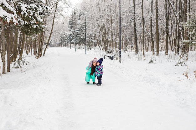 幸せな家族の母と女の赤ちゃんの娘が雪の中で屋外で冬に遊んで笑っています。