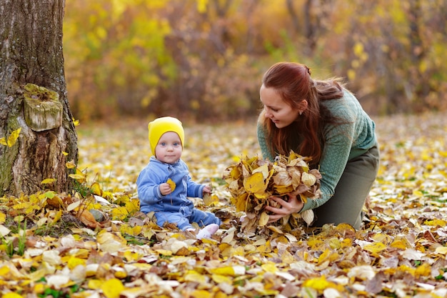 Счастливая семья, мать и ребенок смеются с листьями на природе осенью