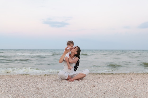 Happy family mother and child daughter doing yoga, meditate in lotus position on beach at sunset