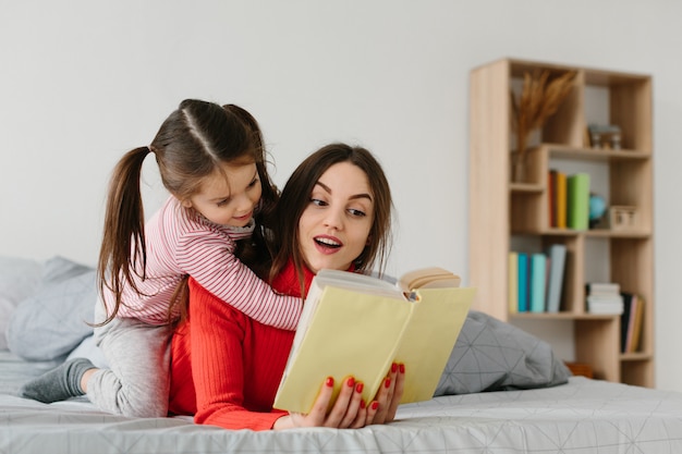 Happy family mother and child daughter reading holding book lying in bed