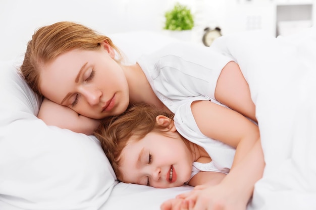 Happy family mother and child daughter sleeping in bed embracing