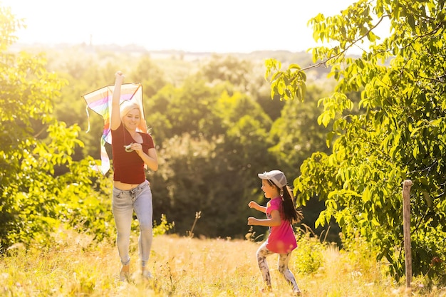 幸せな家族の母と子は自然の夏に凧と牧草地を実行します