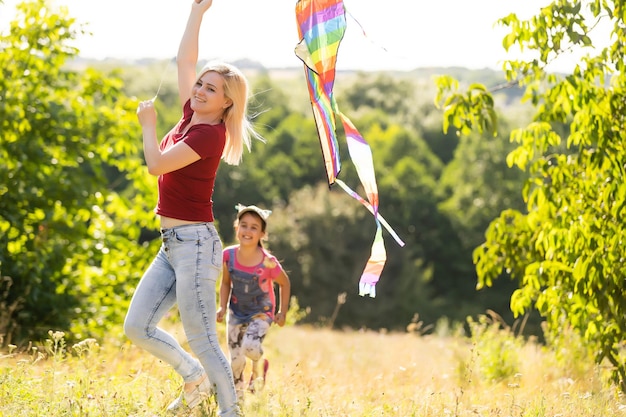 幸せな家族の母と子は自然の夏に凧と牧草地を実行します