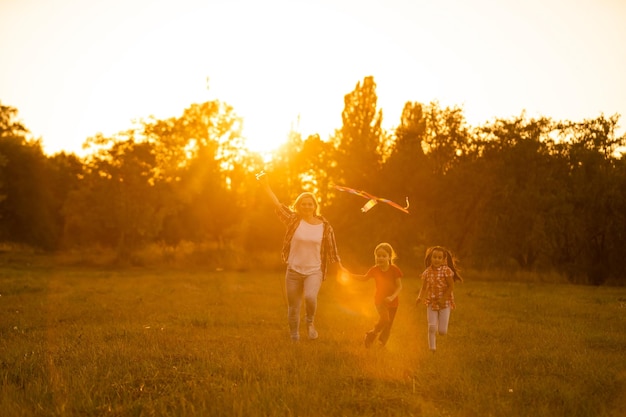 幸せな家族の母と子供たちは自然の中で夏に凧と牧草地を実行します