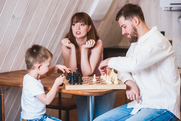 幸せな家族の母父と息子が部屋でチェスをしている