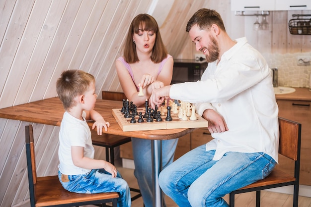 Happy family mother dad and their son playing chess in the room