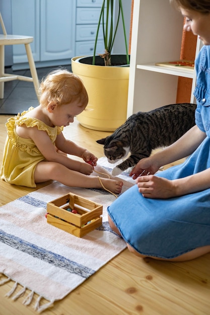 Счастливая семья, мать, дочь и кошка проводят время вместе, играя в материалы марии монтессори