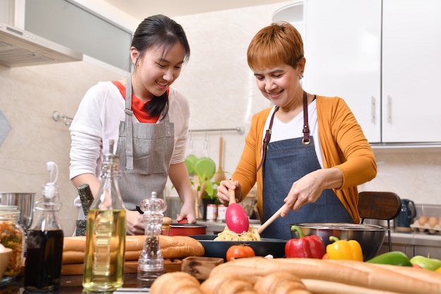 Happy family of mother and daughter cooking in kitchen making healthy food together feeling fun
