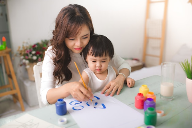 Photo happy family mother and daughter together paint. asian woman helps her child girl.