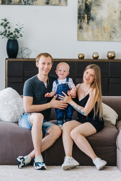 Happy family, mother, father, child, hug each other at home. They are sitting on the sofa in stylish interior. The concept of a happy family.