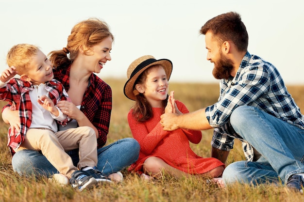 Happy family mother father children son and daughter sit on grass laughing and playing on nature on sunset