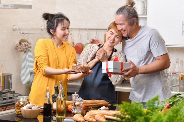 Happy family of mother father and daughter in kitchen celebrating birthday party together with cake and present