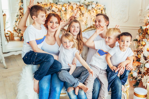 Famiglia felice madre padre cinque figli rilassarsi giocando vicino all'albero di natale