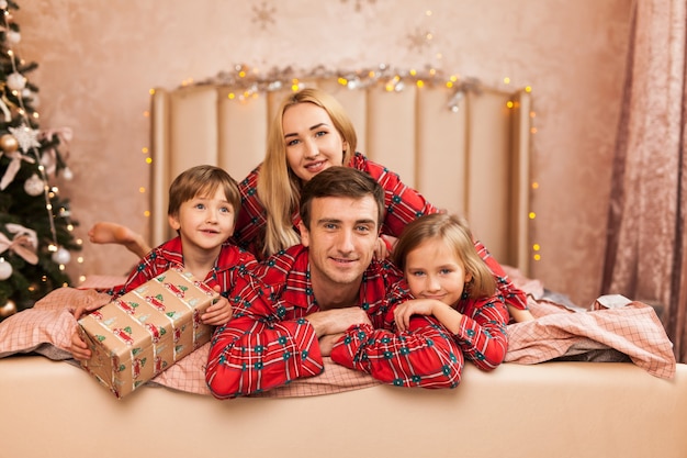 Happy family mother father and kids on Christmas morning in bed in pajamas