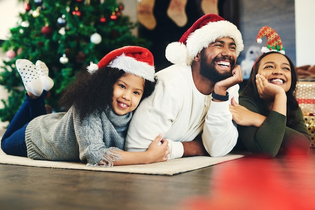 Photo happy family mother and father with child for christmas celebration while relaxing on living room floor at home mom smile and young girl hugging her laughing dad enjoying quality time for bonding