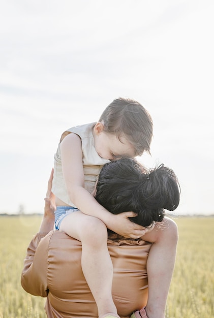 Happy family of mother and infant child walking on wheat field hugging and kissing