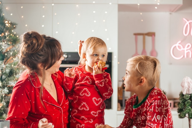 Happy family mother, son and daughter bake cookies for christmas, looking at a little girl