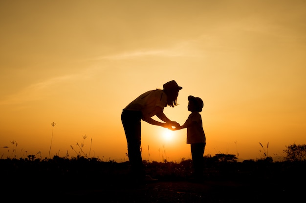 happy family. A mother and son playing in grass fields outdoors at evening silhouette
