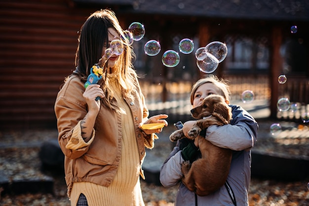 Happy family mother and teen boy son with cute cocker spaniel puppy blow soap bubbles outdoor in