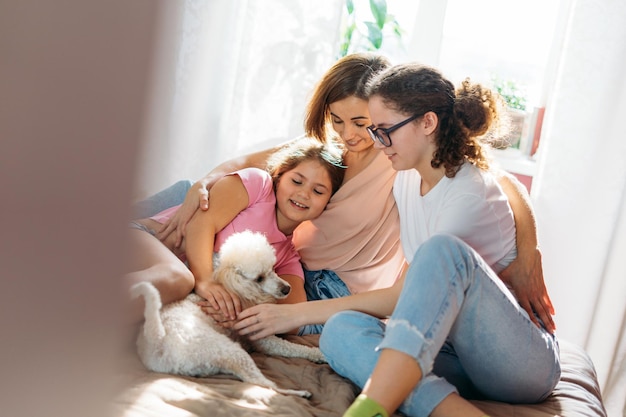 Famiglia felice madre due figlie ragazze e cane barboncino che si divertono insieme a letto in camera a casa