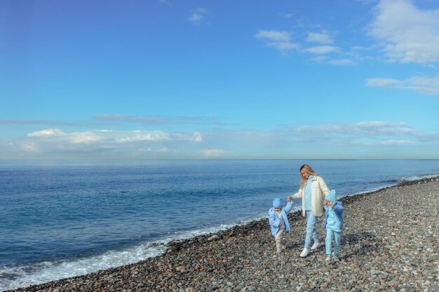 Happy family mother and two daughters walk in warm clothes in autumn or spring along the seashore