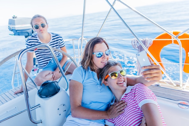 Famiglia felice - madre con adorabili due figlie che riposano e fanno selfie su un grande yacht