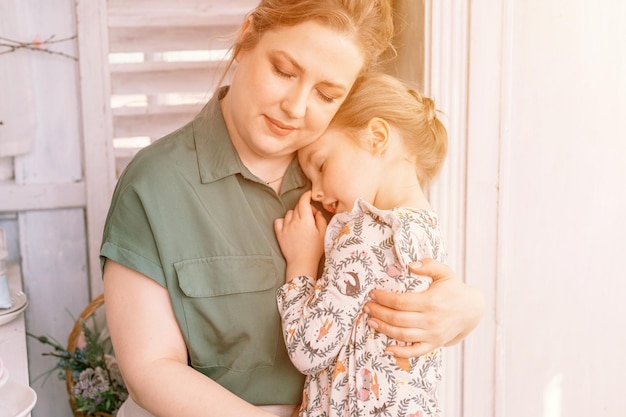 Happy family mother with little kid daughter girl have fun in suburb countryside home life on sunny day candid mom holds child in arms and knees and hugs people love and care moment flare