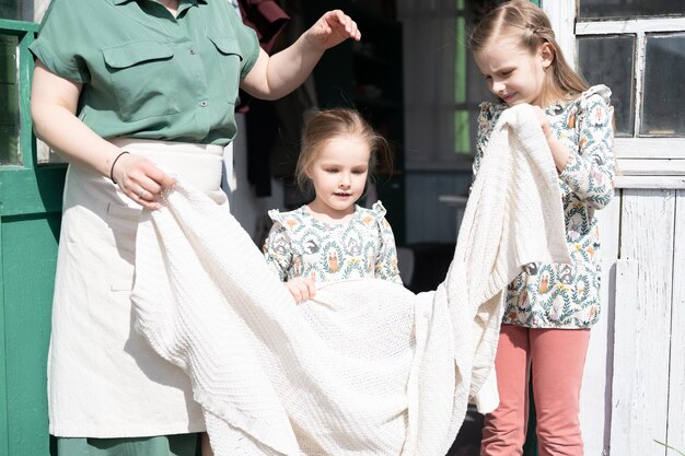 Happy family mother with little kids daughters helper girls
have fun in suburb countryside life on sunny laundry day candid mom
and children doing chores on porch of country house people with
plaid