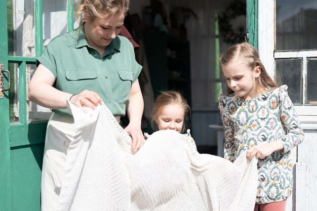 Happy family mother with little kids daughters helper girls have fun in suburb countryside life on sunny laundry day candid mom and children doing chores on porch of country house people with plaid