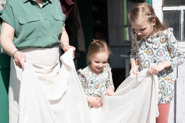 Happy family mother with little kids daughters helper girls
have fun in suburb countryside life on sunny laundry day candid mom
and children doing chores on porch of country house people with
plaid