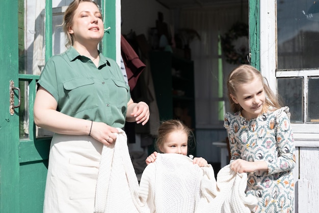 Happy family mother with little kids daughters helper girls
have fun in suburb countryside life on sunny laundry day candid mom
and children doing chores on porch of country house people with
plaid