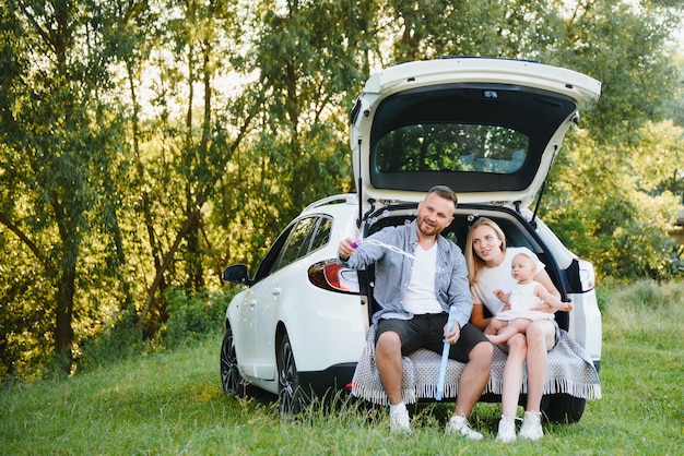 Счастливая семья возле багажника автомобиля в солнечный день. Дорожное путешествие