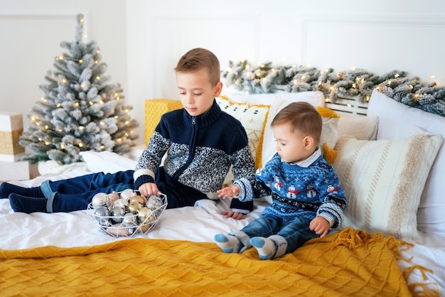 Happy family New Year concept. Two cute smiling kids brothers having fun, playing on the bed with cosy blanket against the Christmas background. New Year and Christmas holidays.