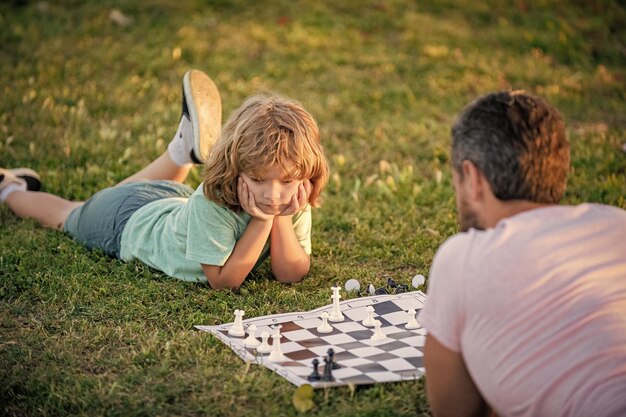 写真 公園の屋外チェスプレーヤーで緑の芝生でチェスをしている親と息子の子供の幸せな家族