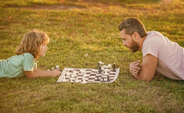 Happy family of parent and son child playing chess on green grass in park outdoor chess game